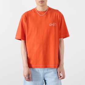 Model wearing Emporium Script Logo T-Shirt in orange with embroidered logo detail, styled with light blue jeans and layered necklace.