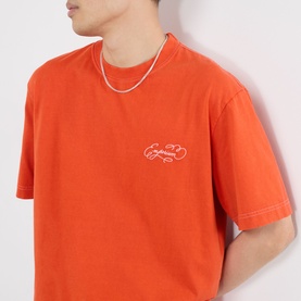 Model wearing Emporium Script Logo T-Shirt in orange with embroidered logo and contrast stitching, styled with a silver chain necklace.