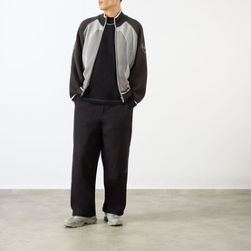 Model wearing Emporium Script Logo T-Shirt in black, styled with grey and black bomber jacket and wide-leg black trousers.