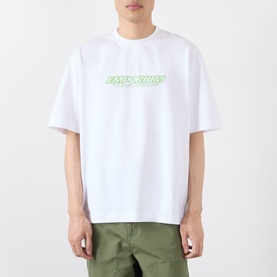 Model wearing Emporium There'll Be Signs Logo T-Shirt in white with green logo print, crew neck, short sleeves, styled with olive trousers.