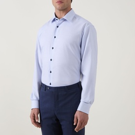 Model wearing Eterna blue cotton formal shirt with navy contrast buttons, single cuff, spread collar, styled with navy trousers