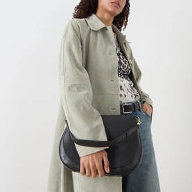Model carrying Gianni Chiarini Helena Round Crossbody Bag in black grained leather with gold-tone hardware, styled with sage coat and jeans