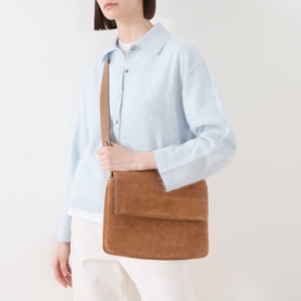 Model carrying Gianni Chiarini Three Flap Suede Crossbody Bag in beige with gold-tone hardware, worn crossbody. Styled with light blue jacket and