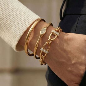 Model with Mettle & Bloom gold bracelets stacked on wrist, featuring chain-link, bangle, and crystal-embellished bar styles