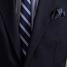 Close-up of navy suit jacket styled with a navy striped tie and white polka dot pocket square