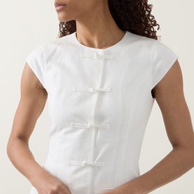 Model wearing Aligne Jennie Shirt Dress in white with knot front fastenings, cap sleeves and round neck, in cotton-linen blend
