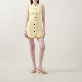 Model wearing Aligne Leah Mini Dress in lemon, sleeveless button-front mini with round neckline, styled with strappy kitten heel sandals.