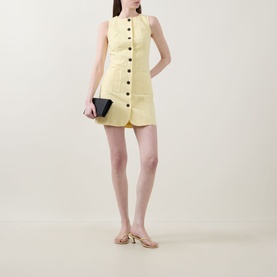 Model wearing Aligne Leah Mini Dress in lemon, sleeveless button-front mini with patch pockets, styled with nude heeled sandals and black clutch bag
