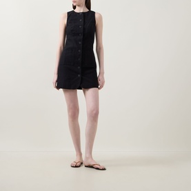 Model wearing Aligne Leah Mini Dress in black, sleeveless linen-blend with button front, styled with brown flip flops.