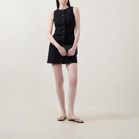 Model wearing Aligne Leah Mini Dress in black; sleeveless linen-blend with front buttons and patch pockets, styled with tan flat sandals.