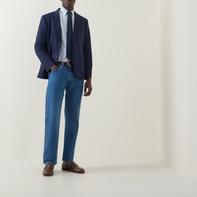 Model wearing Gant Patch Pocket Single-Breasted Blazer in Evening Blue with light blue jeans, white shirt, navy tie and brown loafers.