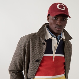 Model with Gant G-Badge Logo Moleskin Cap in Deep Grape Wine, five-panel with G logo. Styled with colour-block rugby shirt and houndstooth coat.