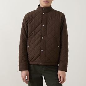 Model wearing Gant Classic Quilted Jacket in black brown with funnel neck and snap buttons, styled with dark green trousers.