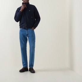 Model wearing Gant Hampshire Shield Logo Jacket in Evening Blue with stand collar, styled with mid-blue straight-leg jeans and dark loafers.
