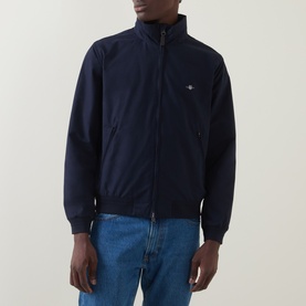 Model wearing Gant Hampshire Shield Logo Jacket in Evening Blue, zip-up with ribbed trims and chest Shield logo, styled with blue jeans.