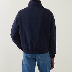 Model wearing Gant Hampshire Shield Logo Jacket in Evening Blue, rear view, styled with light-wash jeans. Ribbed hem and cuffs visible.