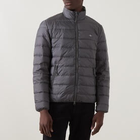 Model wearing Gant Dusky Anthracite quilted casual jacket with funnel neck, small logo badge, and zip pockets, styled with black trousers.