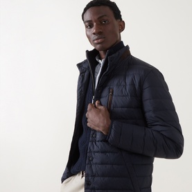 Model wearing Gant Evening Blue quilted casual jacket with tan zip pocket detail, styled with cream trousers and black roll neck