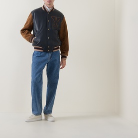 Model wearing Gant Varsity Logo Leather Bomber Jacket in navy with tan sleeves, styled with blue jeans and white trainers.