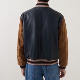 Model wearing Gant Varsity Logo Leather Bomber Jacket in navy with tan suede sleeves and striped ribbed trims, styled with blue jeans. Back view.