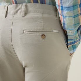 Model wearing Gant Classic Mid-Rise Straight Leg Chinos in clay beige, showing rear zip pocket, logo patch, and button detail, styled with a plaid