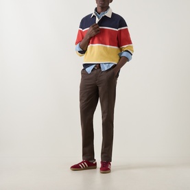 Model wearing Gant Shadow Brown cotton chino trousers, styled with a multicoloured stripe rugby shirt and red suede trainers.