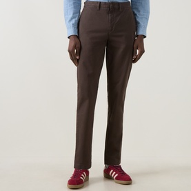 Model wearing Gant Shadow Brown cotton chino trousers, styled with a light blue shirt and red trainers.