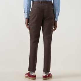Model wearing Gant Shadow Brown cotton chino trousers, rear view, styled with a light blue shirt and red trainers.