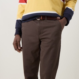 Model wearing Gant Shadow Brown cotton chino trousers with brown leather belt, styled with yellow and navy colour-block sweatshirt.