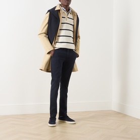Model wearing Gant Evening Blue Chino Jeans with a striped polo, camel trench coat and navy vest, styled with dark trainers.