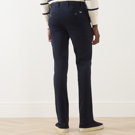 Model wearing Gant Evening Blue cotton chino trousers, rear view, styled with a cream striped jumper and white trainers.