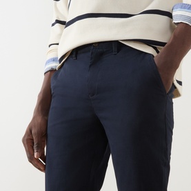 Model wearing Gant Evening Blue cotton chino trousers, styled with a striped cream knit and blue shirt.