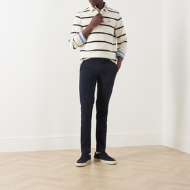 Model wearing Gant Evening Blue cotton chino trousers, styled with a cream stripe polo shirt and navy canvas shoes.