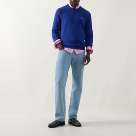 Model wearing Gant Shield Logo Sweater in Crisp Blue crew neck knit, styled with a pink shirt and light blue jeans.