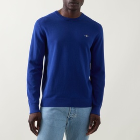 Model wearing Gant Shield Logo Sweater in Crisp Blue, crew neck cotton knit with chest logo embroidery, styled with light blue jeans.