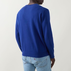 Model wearing Gant Shield Logo Sweater in crisp blue cotton, rear view, styled with light wash jeans.