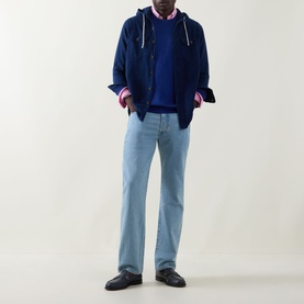 Model wearing Gant Shield Logo Sweater in Crisp Blue crew neck, styled with navy hoodie, striped shirt, light blue jeans and dark loafers.