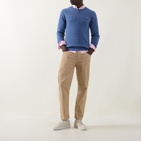 Model wearing Gant Shield Logo Cable-Knit Sweater in Blue Horizon with pink shirt, styled with beige chinos and white trainers.