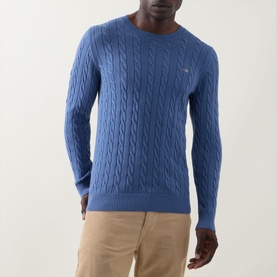 Model wearing Gant Shield Logo Cable-Knit Sweater in Blue Horizon, crew neck, cable-knit cotton. Styled with beige chinos.