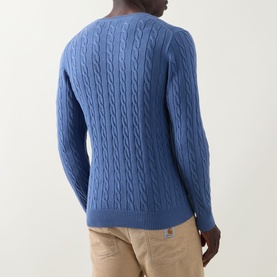 Model wearing Gant Shield Logo Cable-Knit Sweater in Blue Horizon, showing cable-knit back detail and ribbed hem, styled with beige chinos.