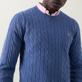 Model wearing Gant Shield Logo Cable-Knit Sweater in Blue Horizon, crew neck, cable-knit cotton, styled with a pink shirt underneath