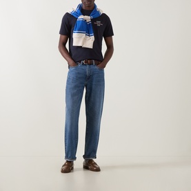 Model wearing Gant Evening Blue Crew Neck T-shirt with blue striped scarf, mid-wash jeans and brown leather shoes.