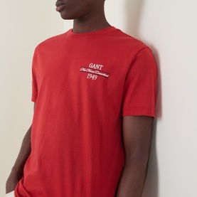 Model wearing Gant 1949 Logo T-Shirt in Maple Fire red, featuring embroidered chest logo, crew neck, and short sleeves.
