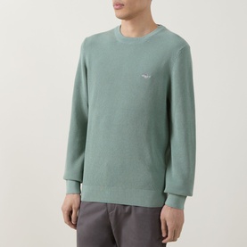 Model wearing Gant Surplus Mint crew neck knit sweater with small logo embroidery, styled with grey trousers.