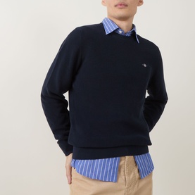 Model wearing Gant Shield Logo Micro Textured Sweater in Evening Blue crew neck, styled over a blue striped shirt with chinos.