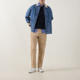 Model wearing Gant Shield Logo Micro Textured Sweater in Evening Blue, styled with denim jacket, checked shirt, and beige trousers.
