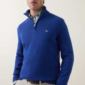Model wearing Gant Shield Logo Half-Zip Sweater in Crisp Blue with embroidered logo, half-zip neck. Styled with a check shirt.