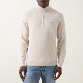 Model wearing Gant Shield Half-Zip Sweater in clay beige, half-zip neckline, ribbed trims and embroidered logo, styled with blue jeans.