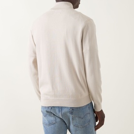 Model wearing Gant Shield Half-Zip Sweater in clay beige, rear view showing ribbed hem, styled with light blue jeans.