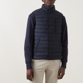 Model wearing Gant Evening Blue quilted gilet with knit sleeves, styled with beige trousers.